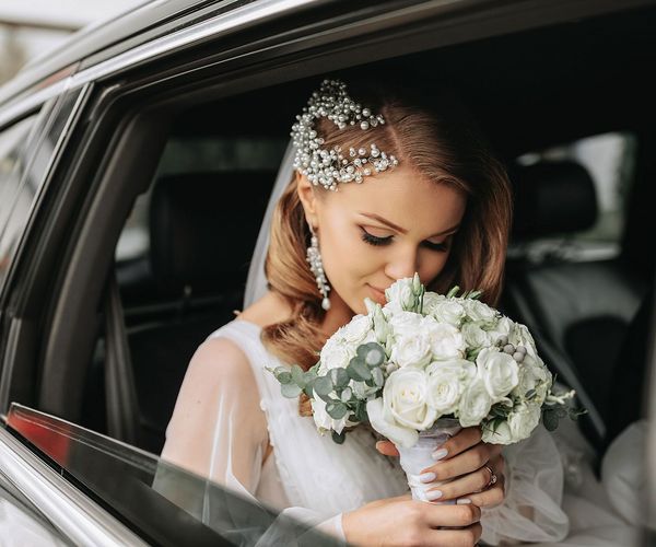 Bride smelling white rose bouquet in a Asheville Premier Transportation limousine, wearing a veil and headpiece.