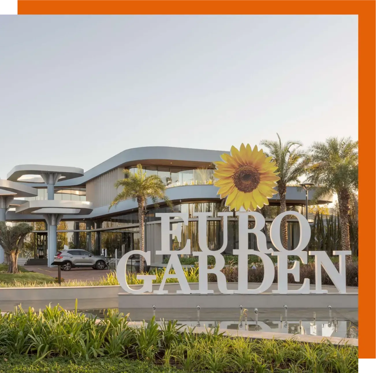 Fachada da loja Euro Garden com placa de girassol, prédio moderno e palmeiras ao lado de uma estrada.