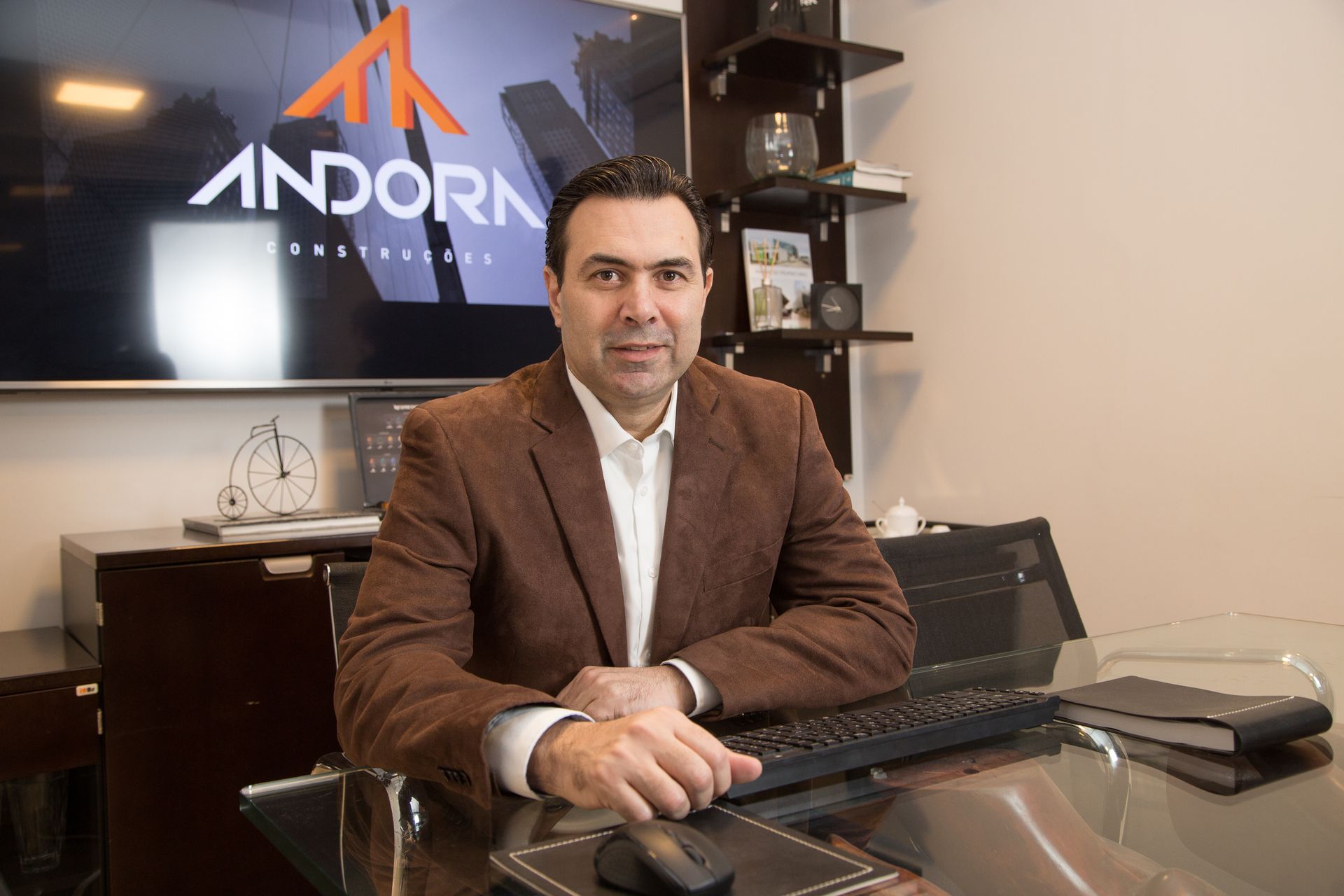 Homem sentado em uma mesa em um escritório com o logotipo da ANDORI na parede, de frente para a câmera.