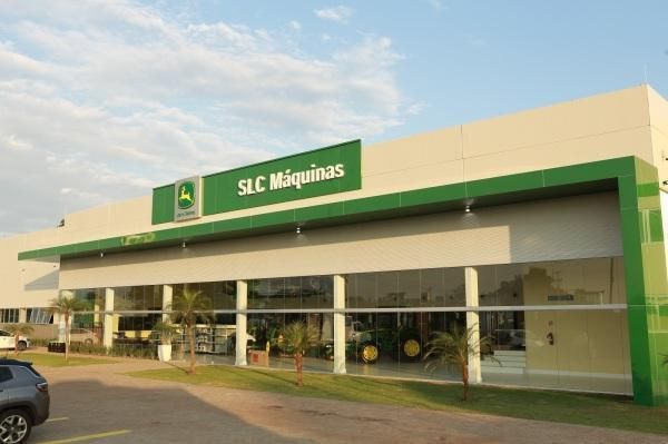 Exterior da loja SLC Máquinas com sinalização verde e fachada de vidro ao pôr do sol