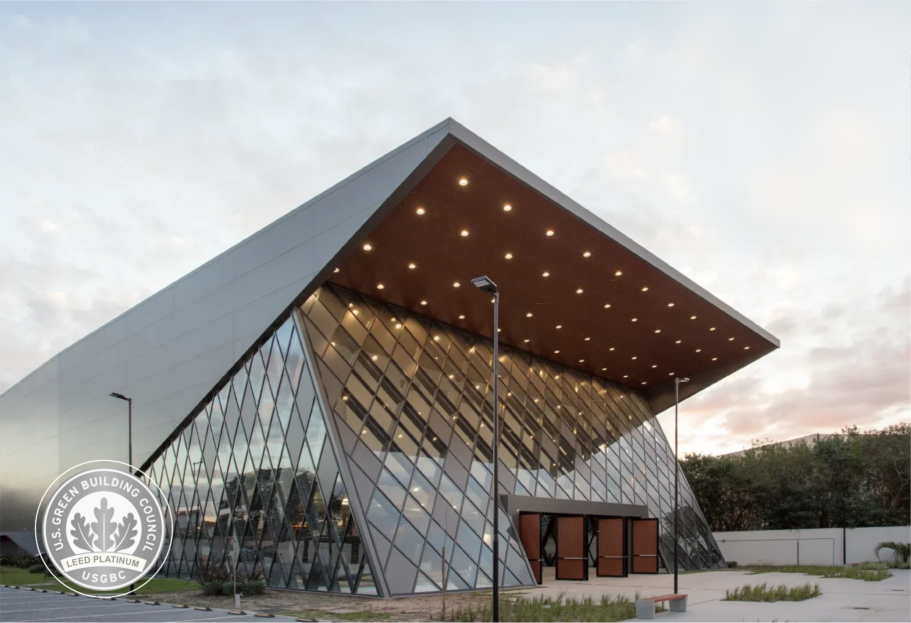 Edifício moderno de vidro com ângulos acentuados e telhado inclinado ao entardecer.