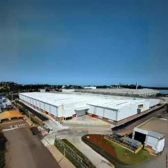 Vista aérea de um grande complexo de armazéns brancos com ruas pavimentadas e céu azul.