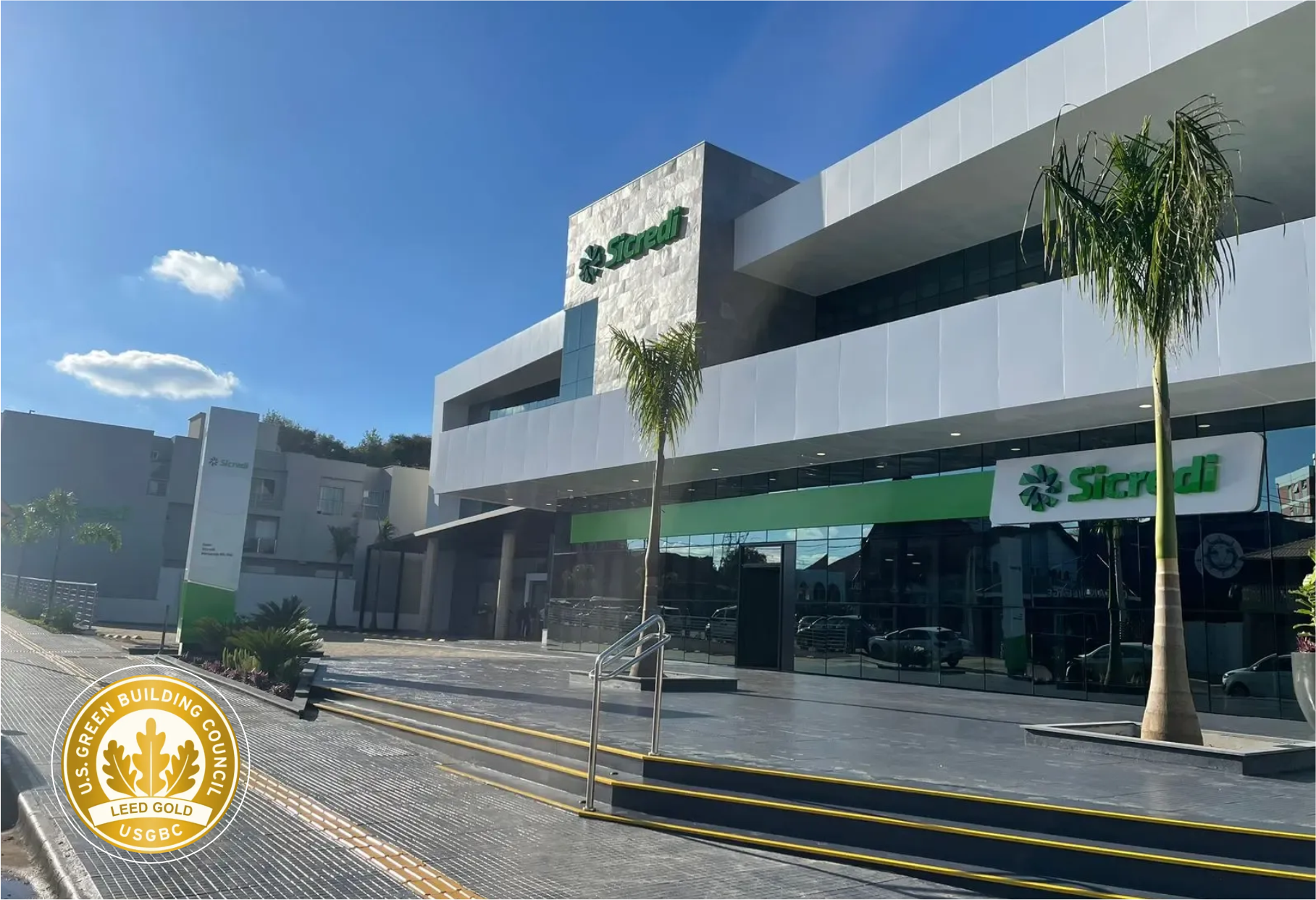 Loja moderna com vitrines de vidro, fachada branca e palmeiras ao longo de uma rua ensolarada.