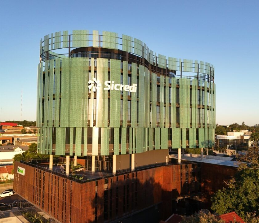 Moderno edifício de escritórios envidraçado com o logotipo da Sicredi, visto de cima ao pôr do sol.