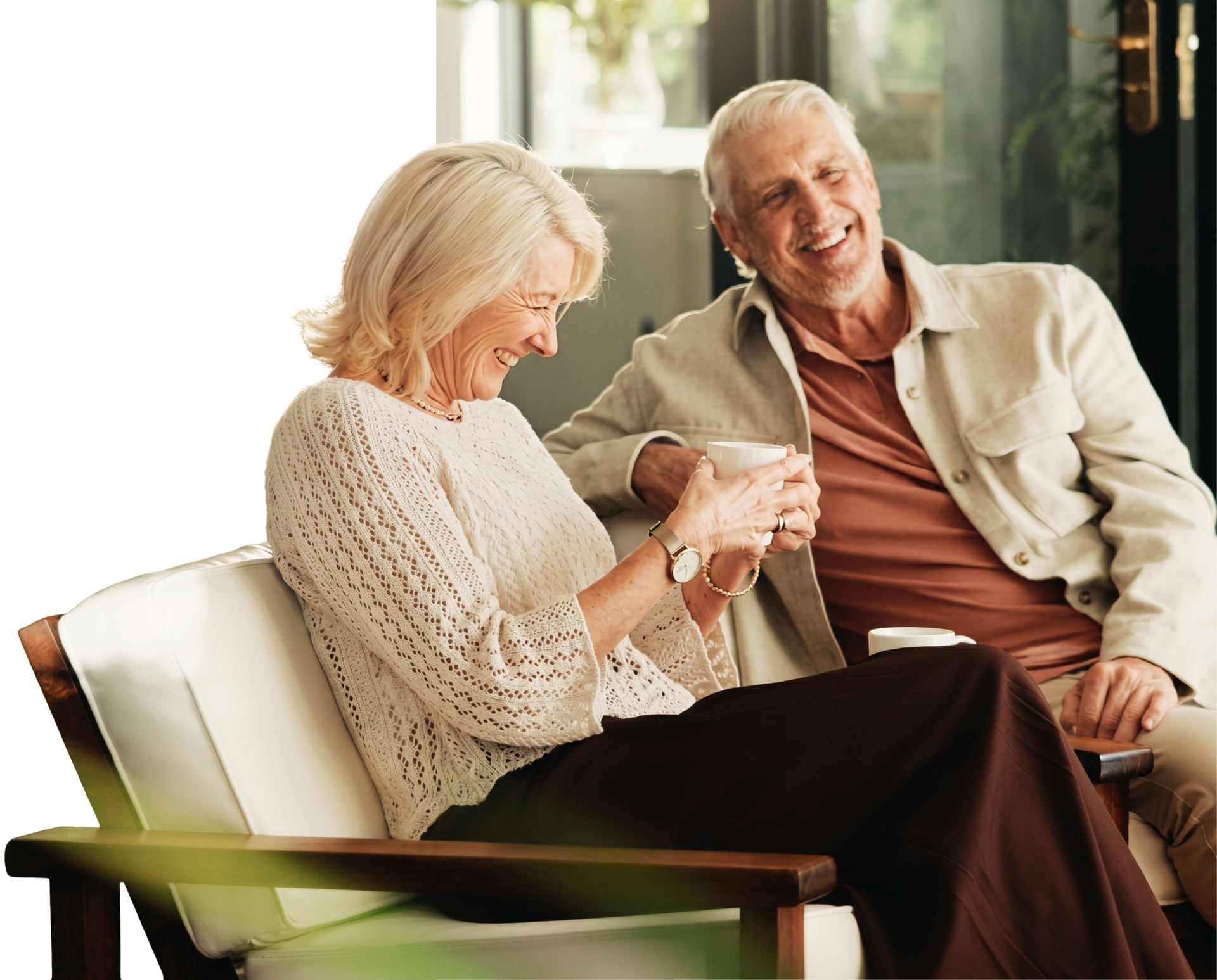 Duas pessoas sorridentes conversando em uma varanda, uma delas segurando uma xícara, sob a luz quente do dia.