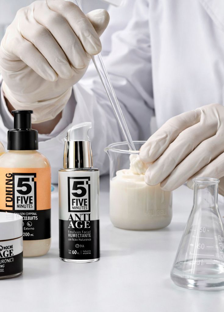 Manos enguantadas usando una pipeta con frascos de productos para el cuidado de la piel .