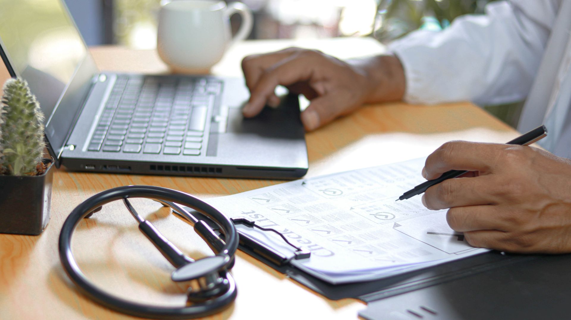 Doctor working on laptop with stethoscope and paperwork on a desk