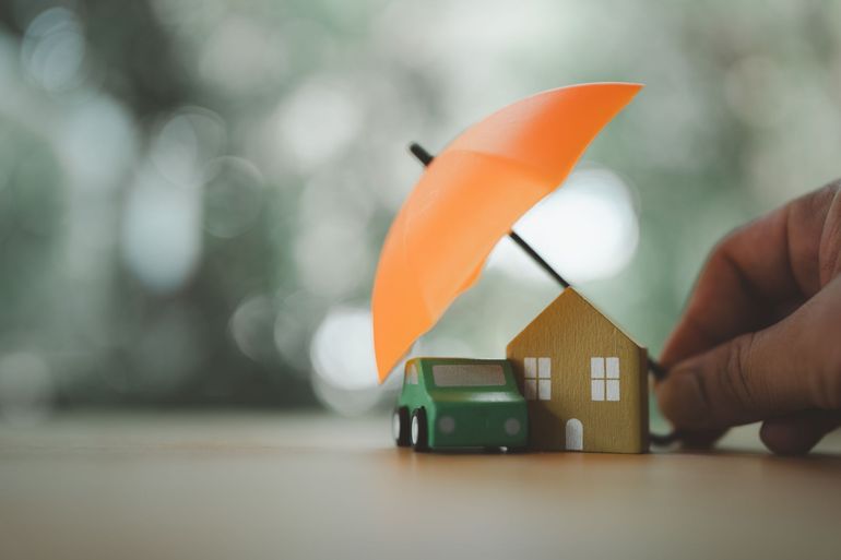 Hand holding a miniature house with an orange umbrella on a table