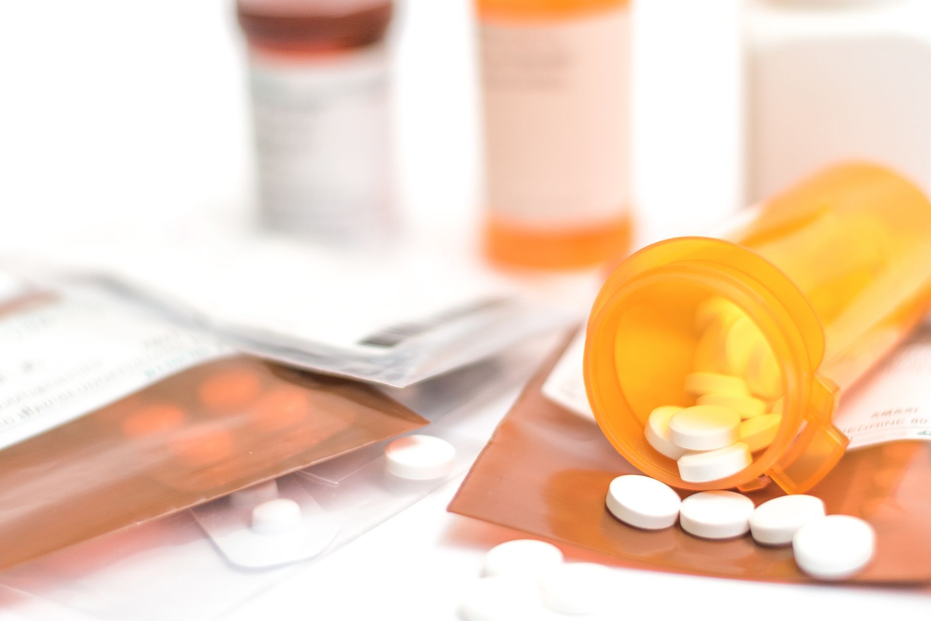 Orange prescription bottle tipped over with white pills spilled on a table, with blurred medicine containers in background