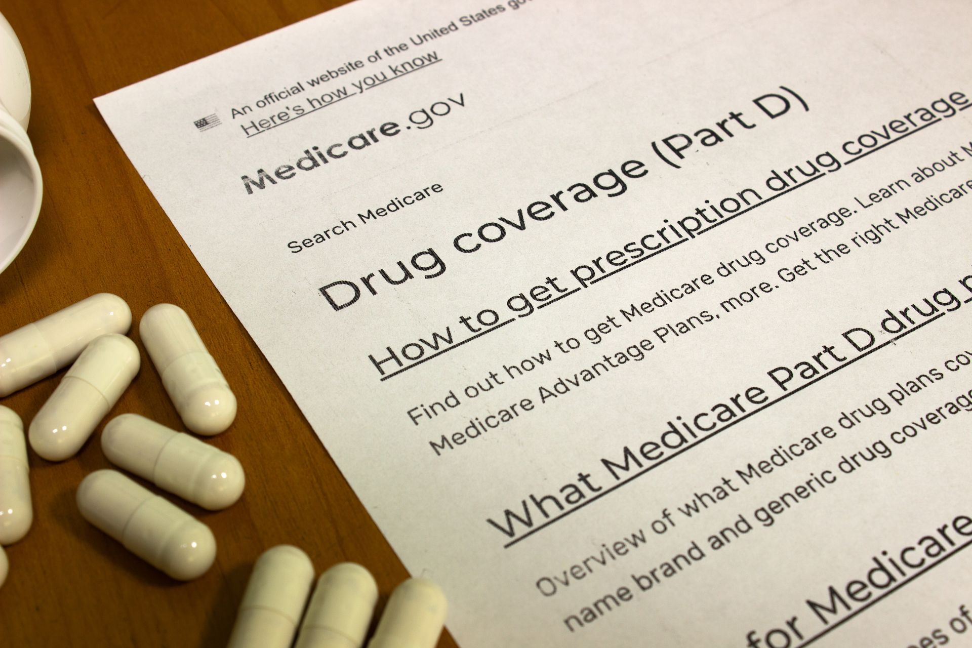 Medicare Drug Coverage document beside white capsules on a wooden table