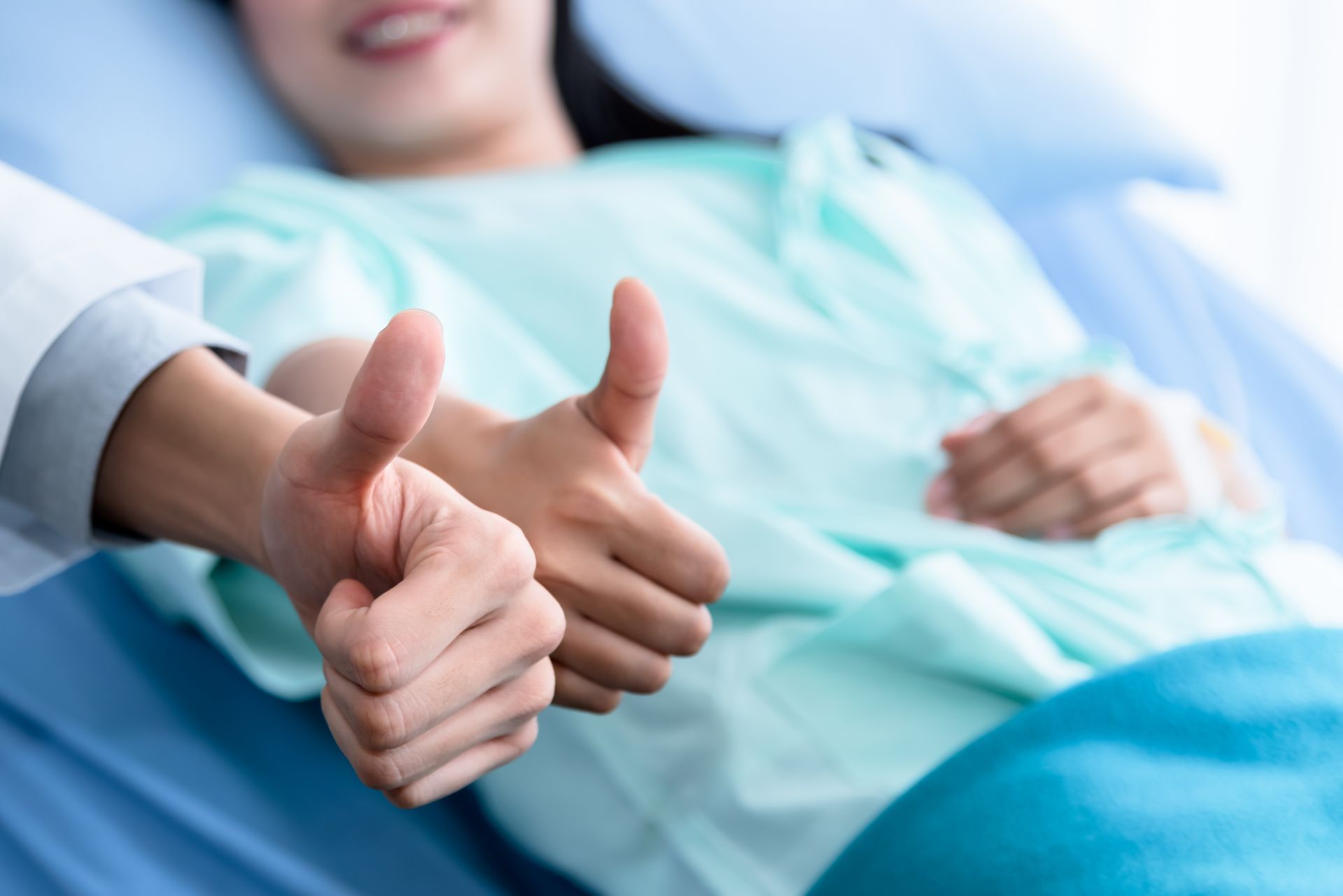 Thumbs-up gesture beside a smiling patient in a hospital bed under a blue blanket