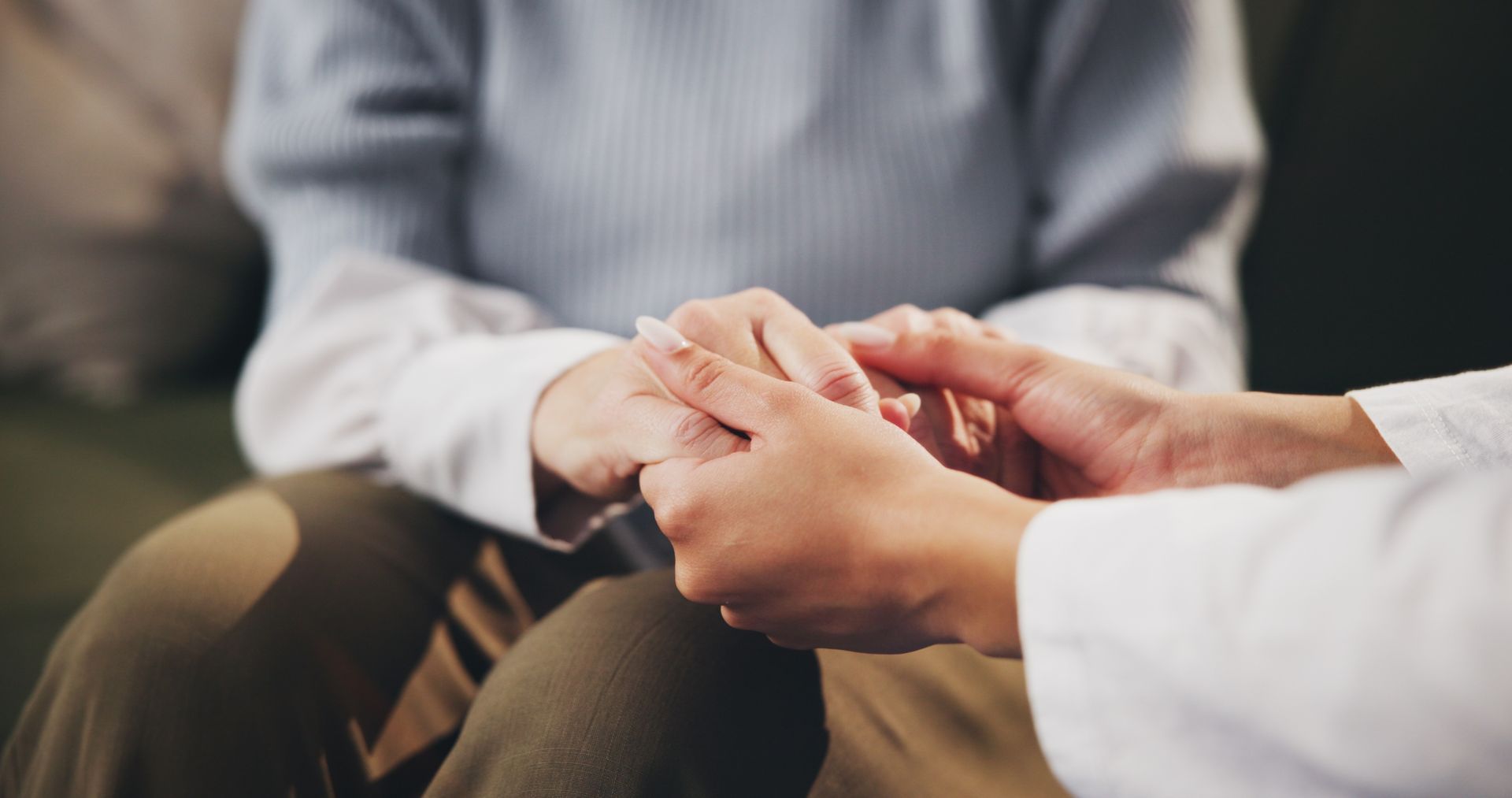 Two people seated, gently holding hands in a comforting gesture.