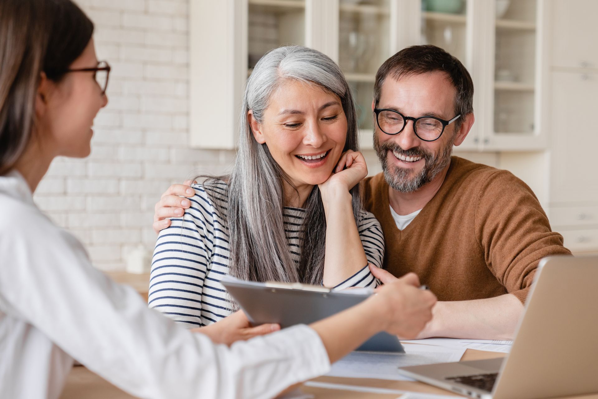 Three people smiling around a laptop in a bright office meeting