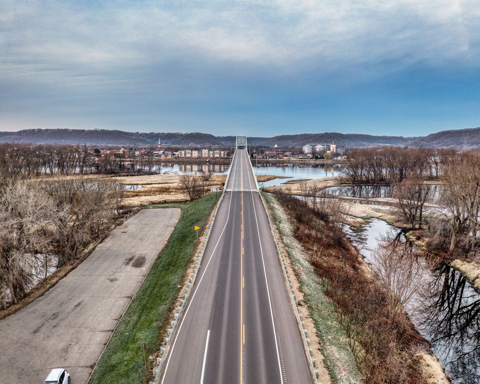 A straight two-lane road stretches through a rural winter landscape under a cloudy sky.