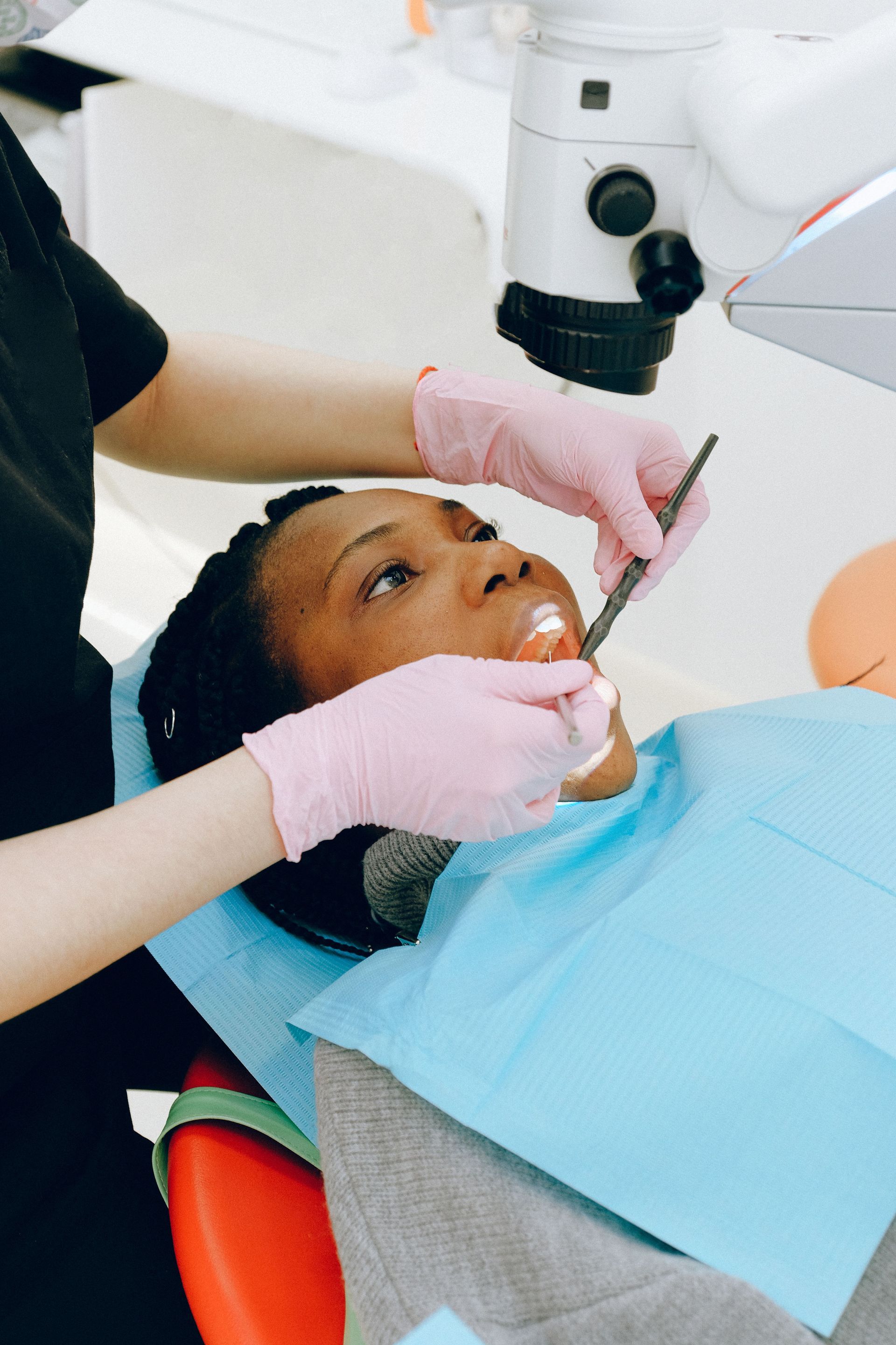 Dentist using pink gloves and a tool to examine a patient reclined in a dental chair