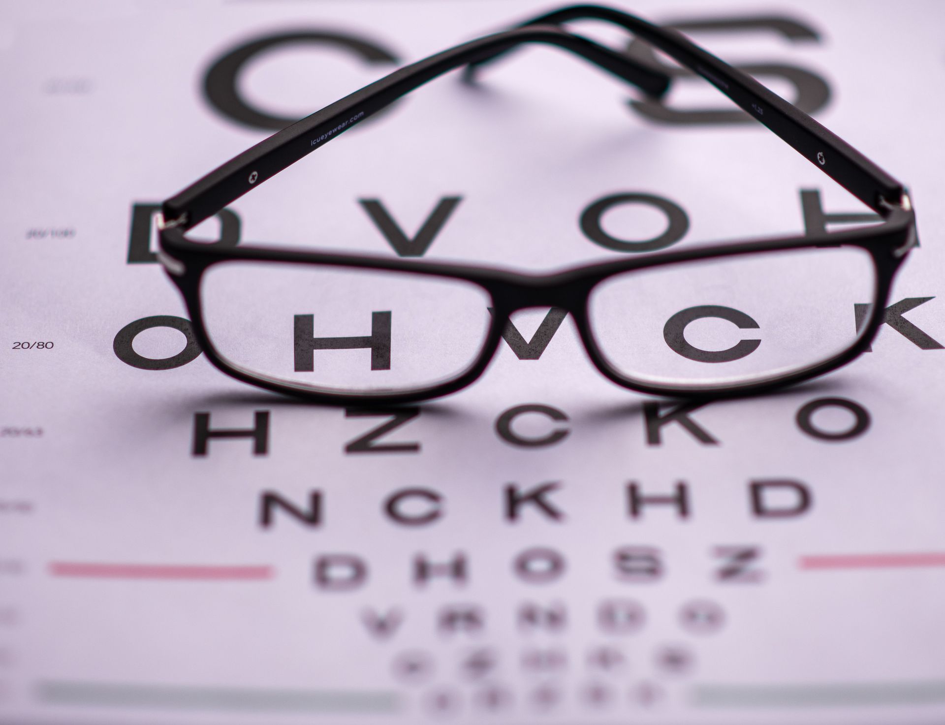 Eyeglasses resting on an eye chart, with letters visible through the lenses