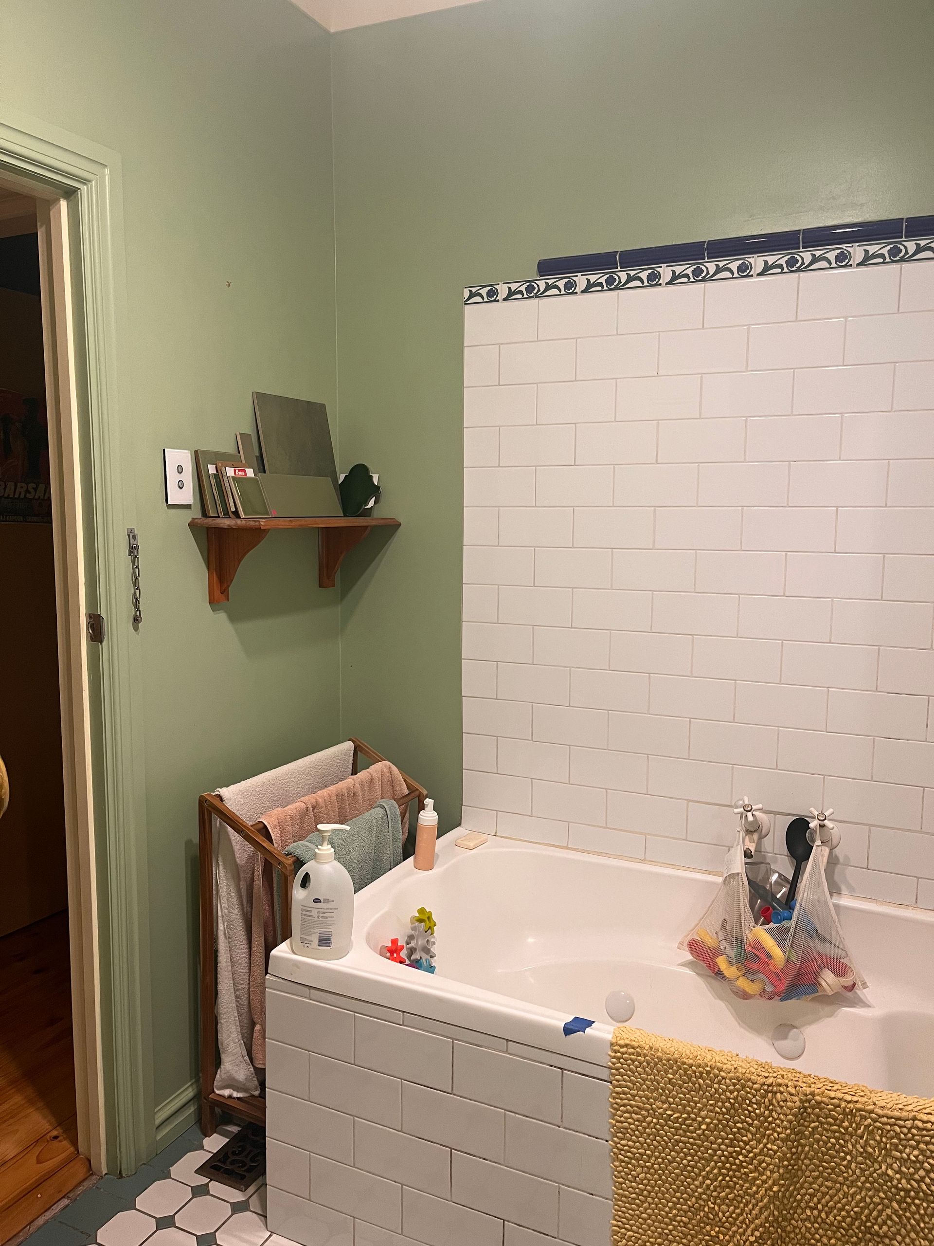 Small bathroom with a white tiled bathtub, green walls, and a towel hanging nearby.