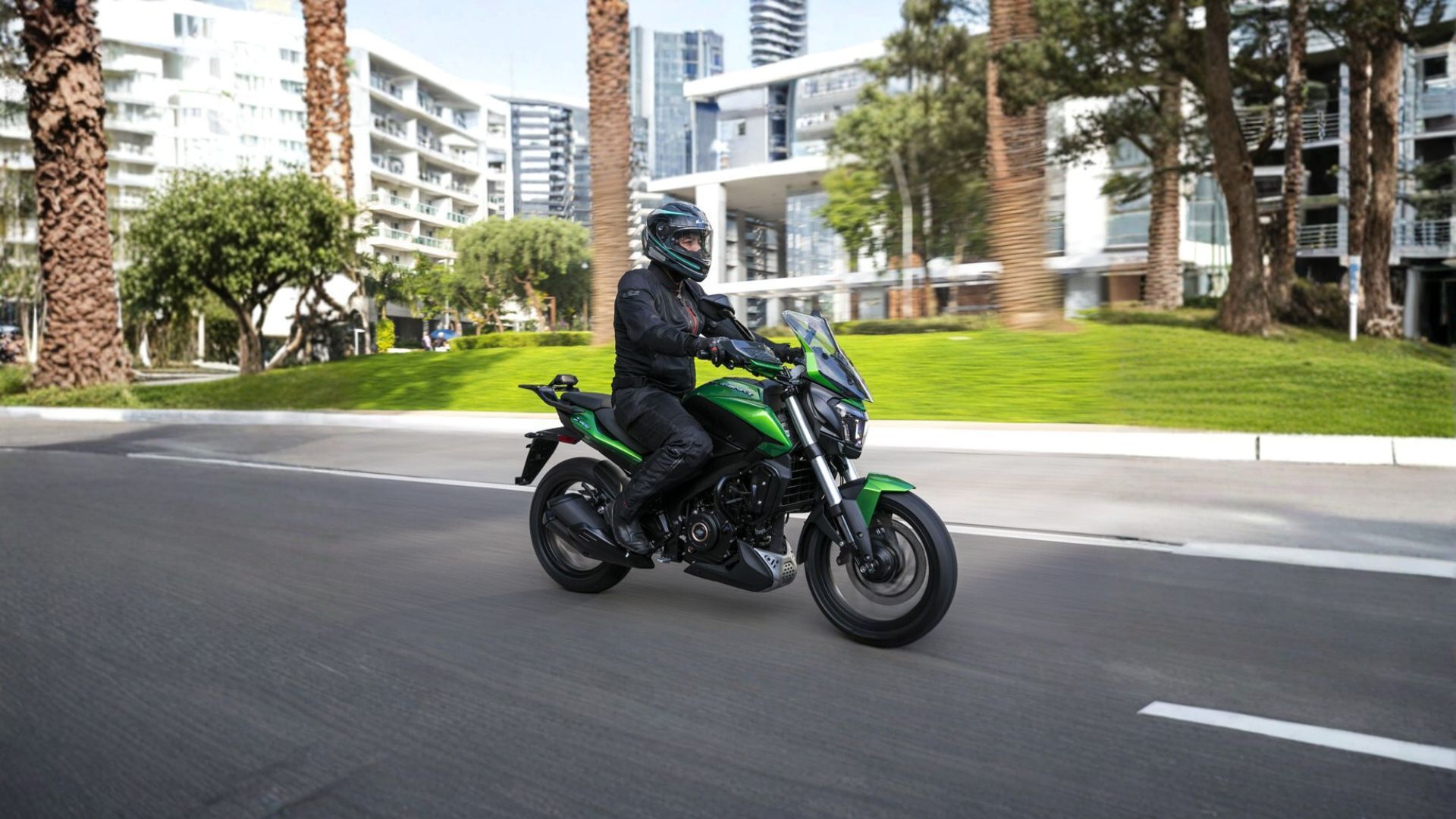Motorcyclist riding a green sport bike on a city street near modern apartment buildings.