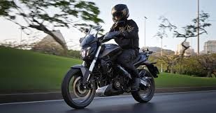 Motorcyclist in black gear riding on a road beside a green lawn at dusk