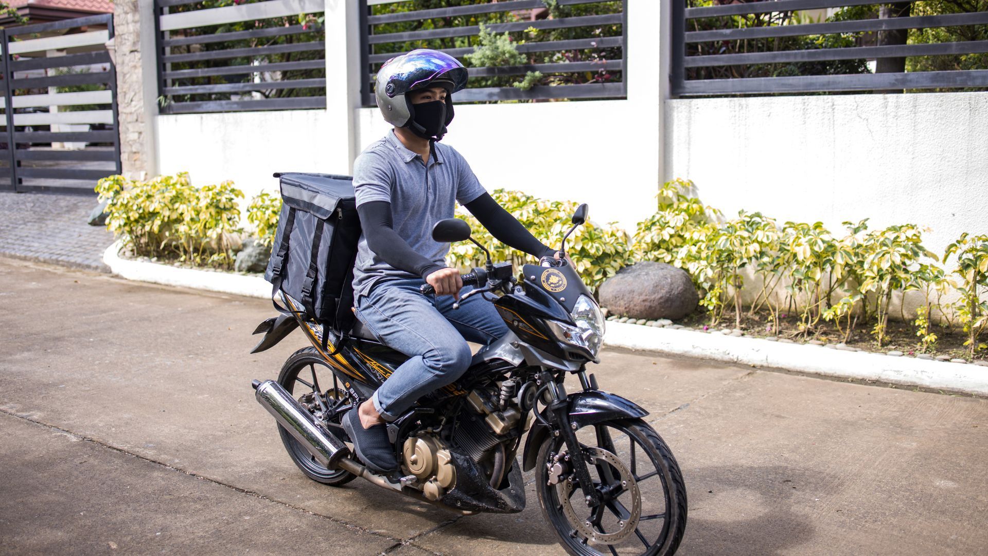Delivery rider on a motorcycle with stacked cargo boxes, riding along a residential street.