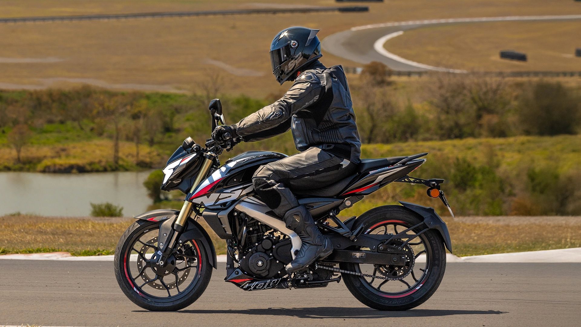 Motorcyclist in black gear riding a black sport bike on a rural road by water and dry hills