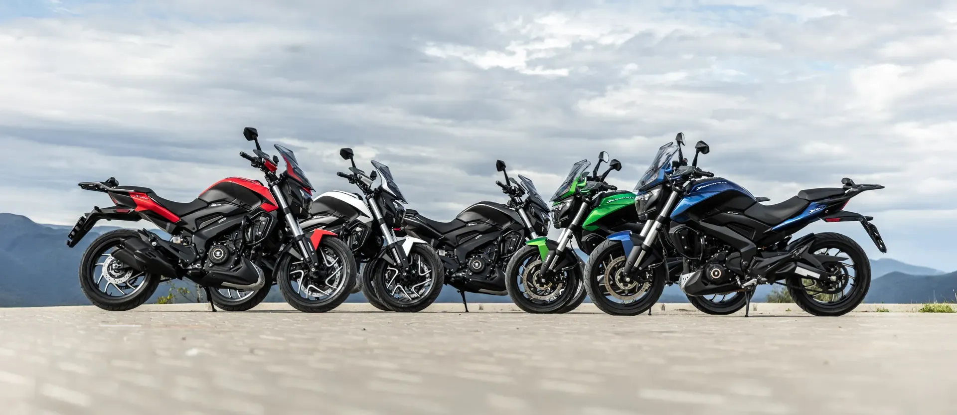 Five sport motorcycles lined up on a road, with mountains in the background.
