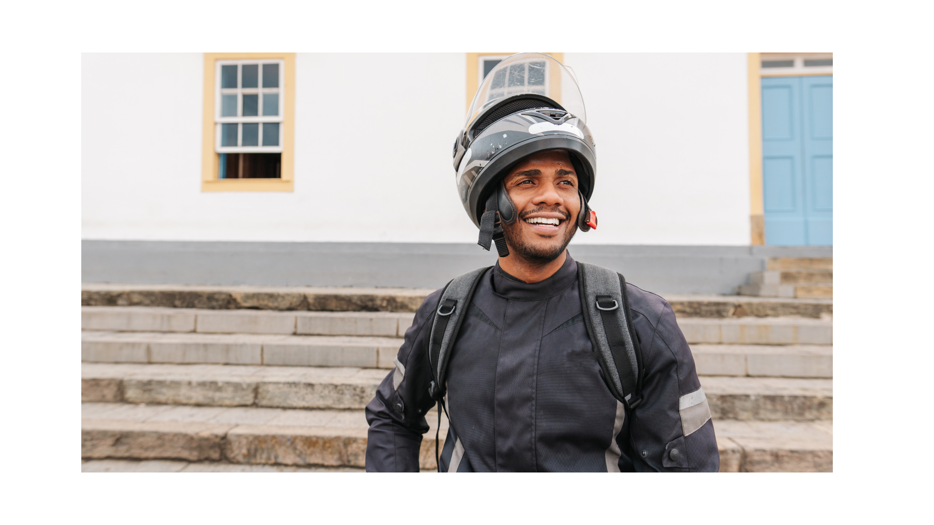 Smiling man in a helmet and backpack standing on steps in front of a building