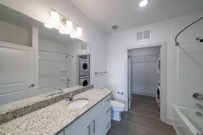 Bathroom with a granite countertop vanity, toilet, bathtub, and a closet with a washer/dryer.