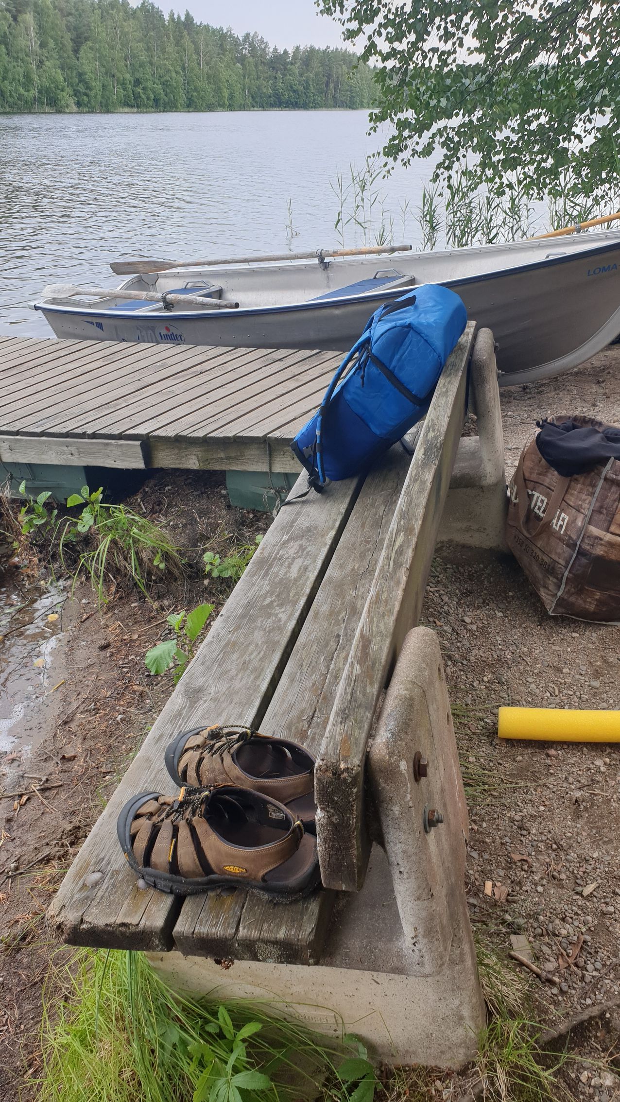 A pair of sandals are sitting on a wooden bench next to a boat.