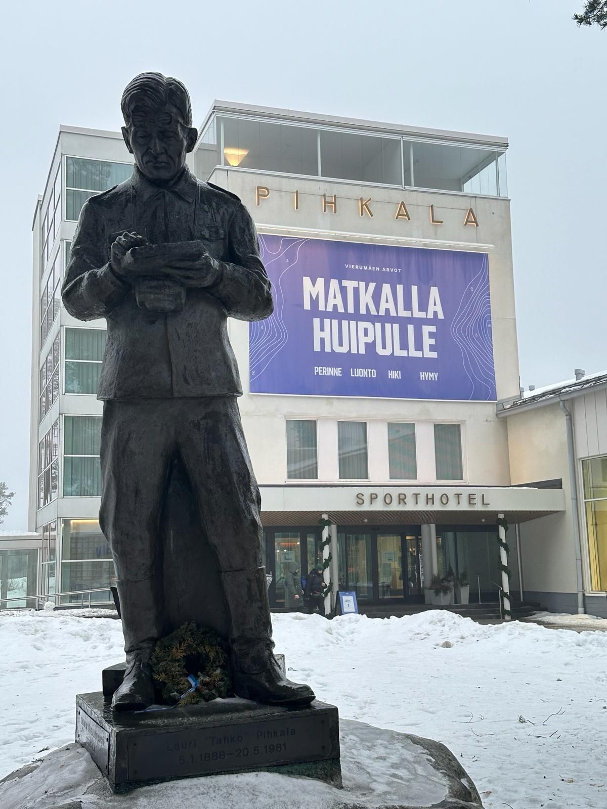 A statue of a man standing in front of a building with a sign that says matkalla huipulle.