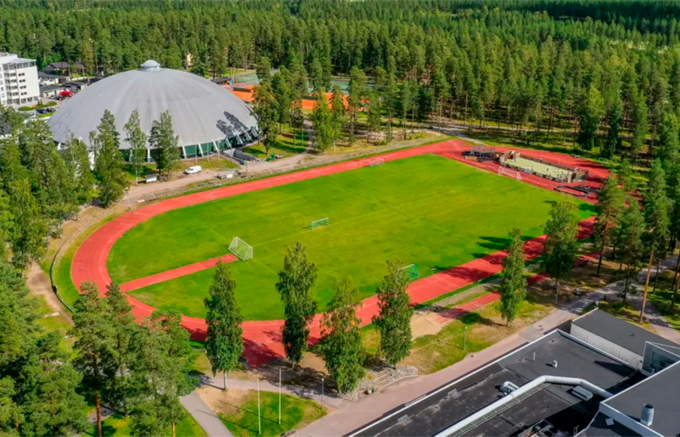 An aerial view of a track and field surrounded by trees and buildings.