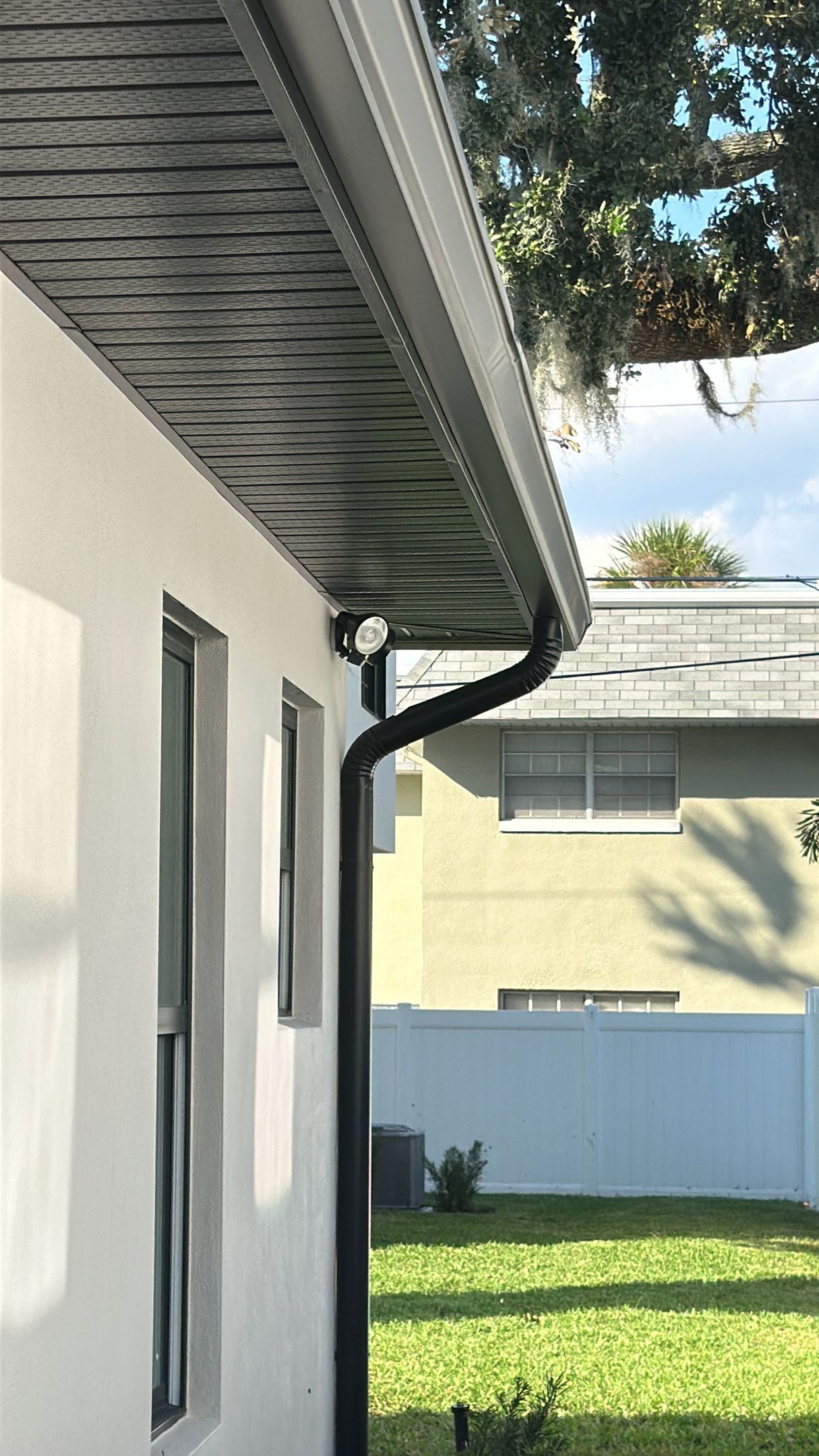 A white house with a black gutter on the side of it.