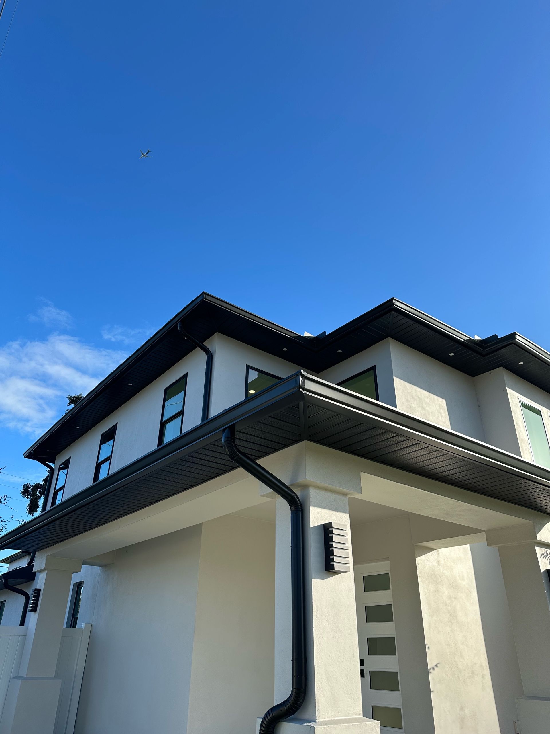 A white house with a black gutter and a blue sky in the background.