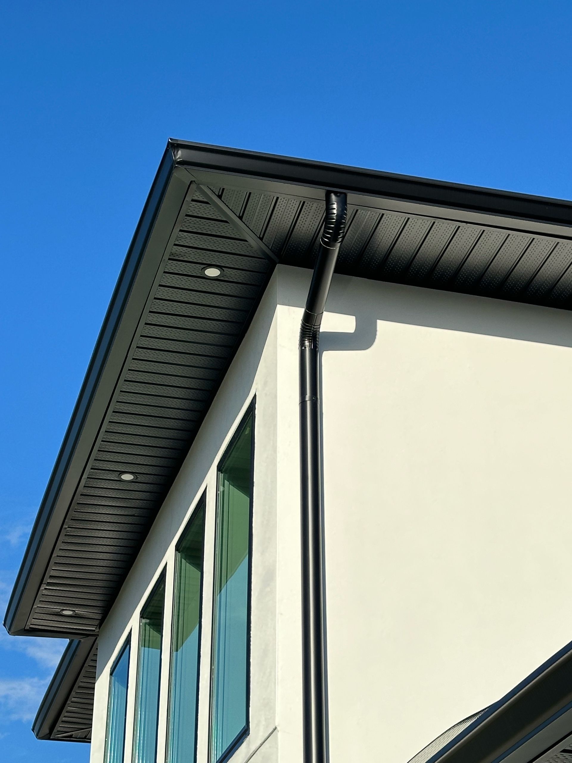 A white house with a black gutter and a blue sky in the background