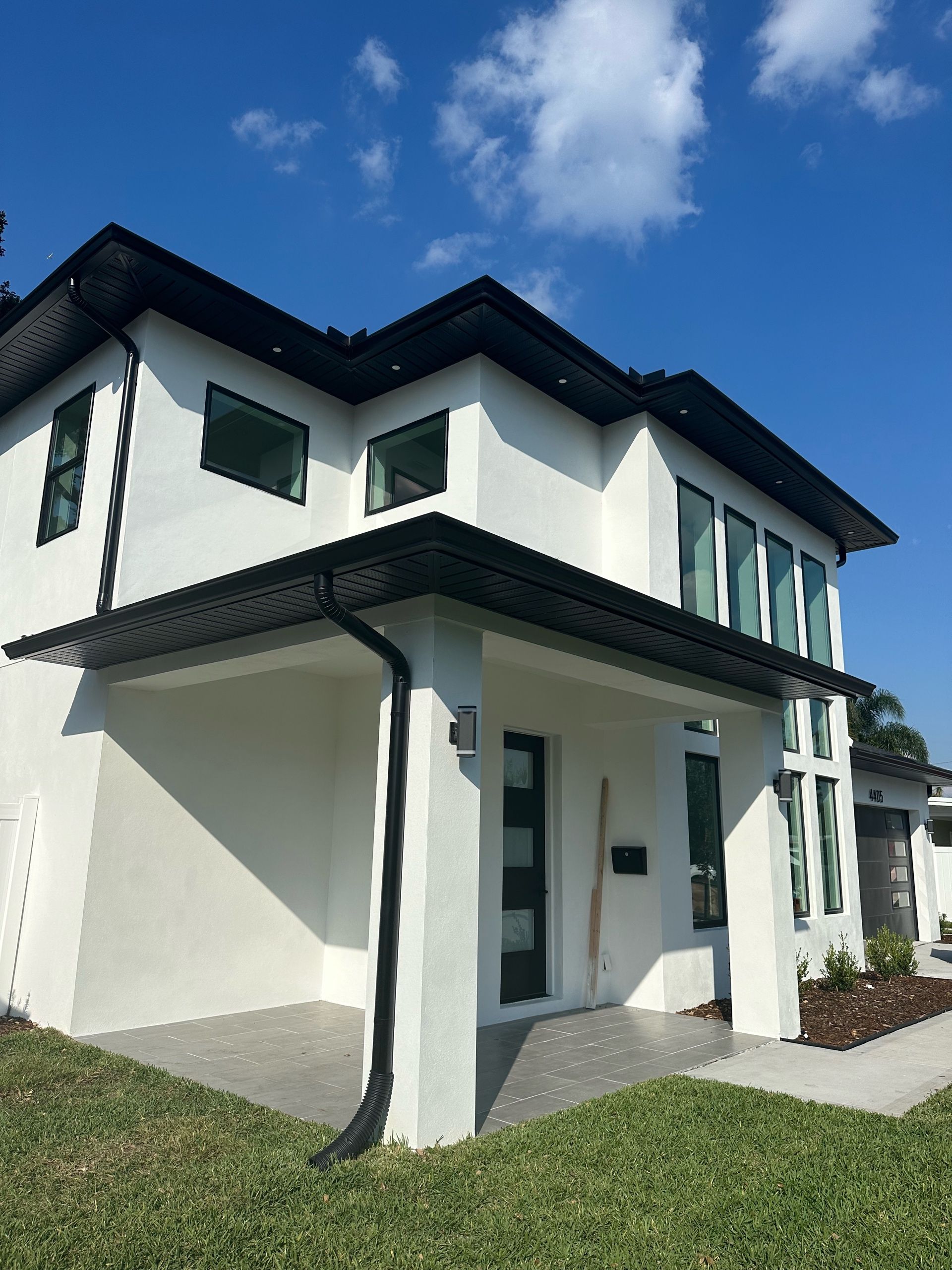 A white house with a black roof is sitting on top of a lush green lawn.