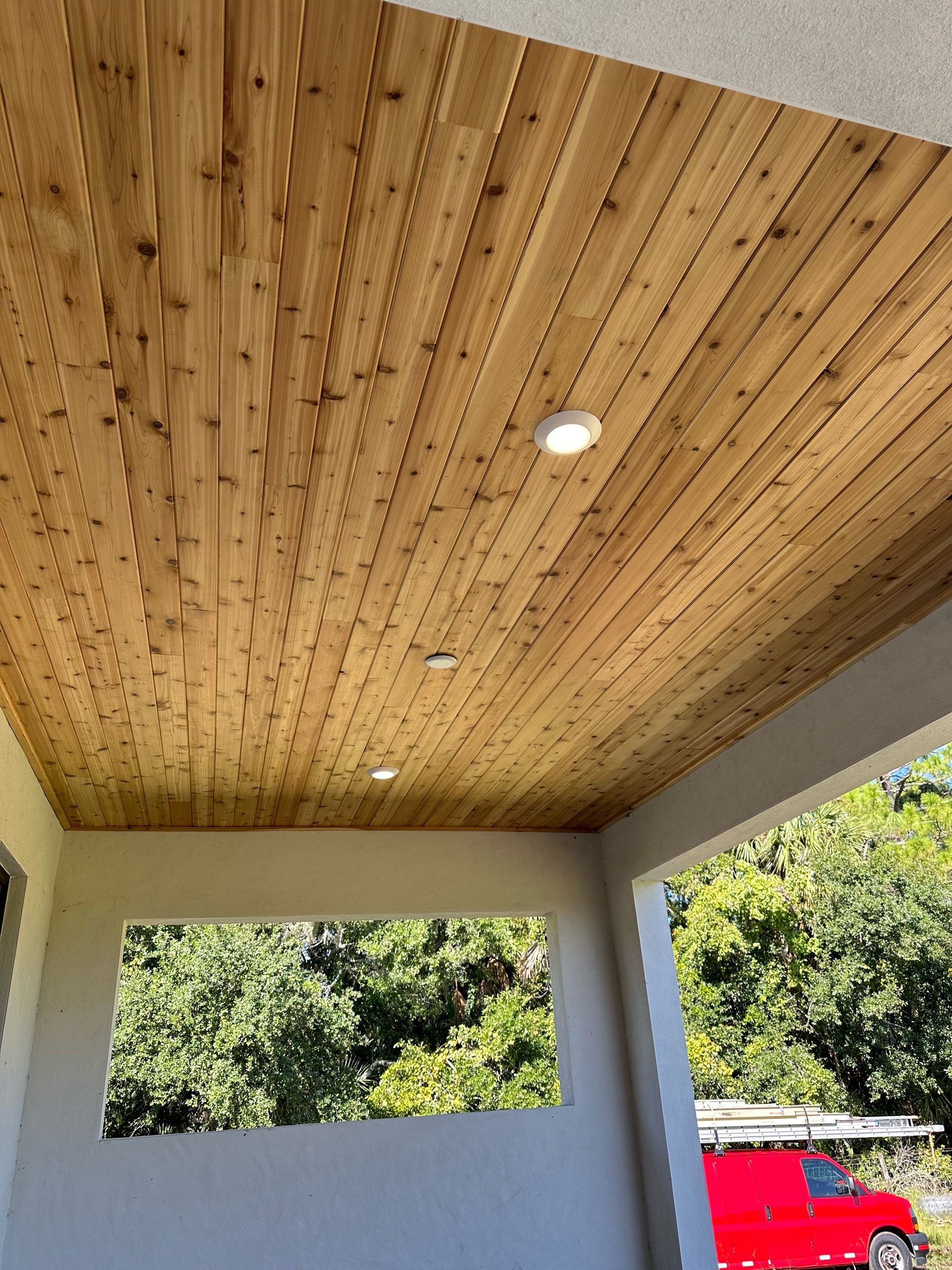 A wooden ceiling on a porch with a red truck in the background.