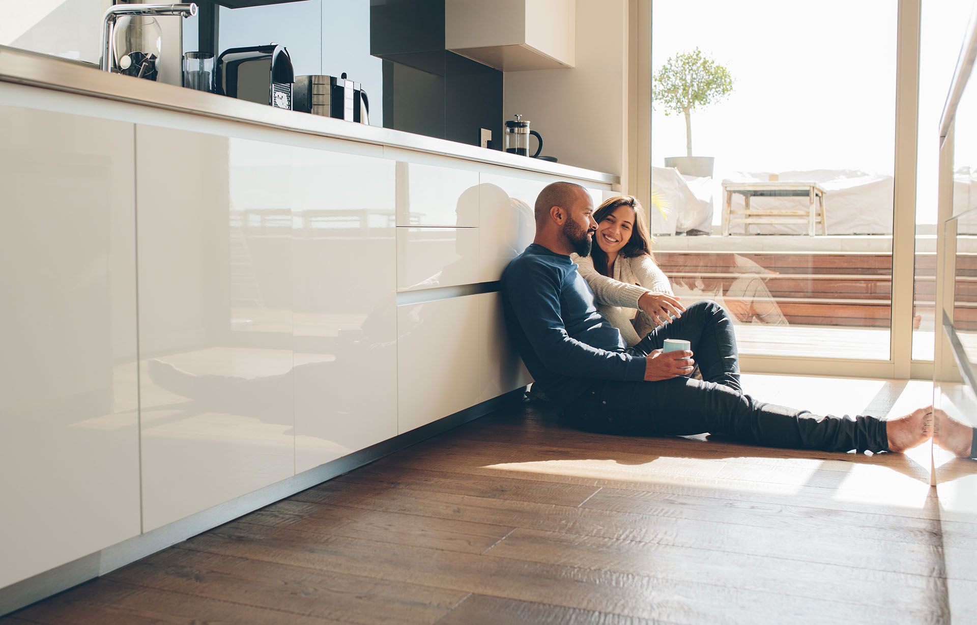 Two people sitting on a kitchen floor beside white cabinets, in bright sunlight. Two people sitting on a kitchen floor beside white cabinets, in bright sunlight.