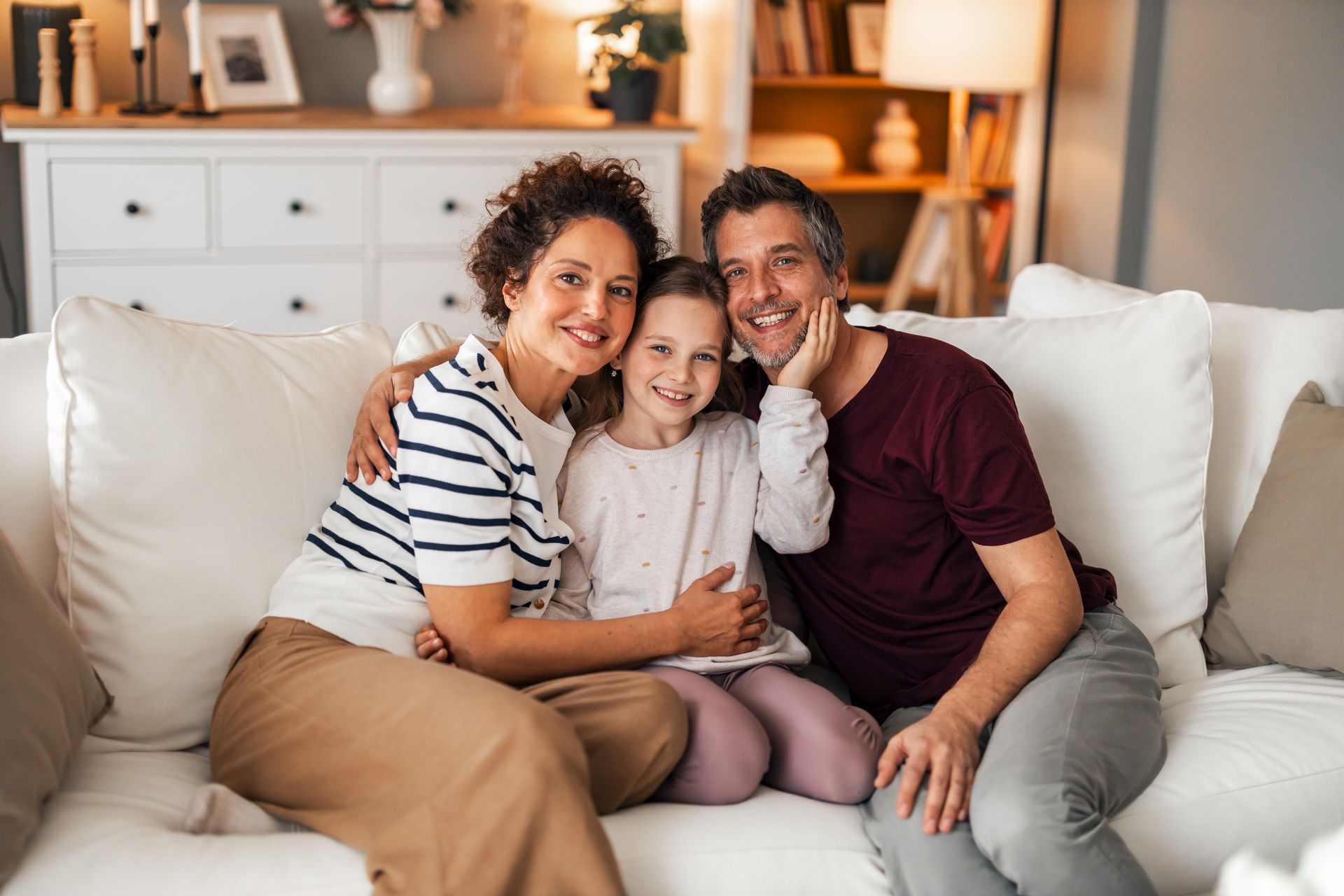 Smiling family sitting together on a white couch in a cozy living room