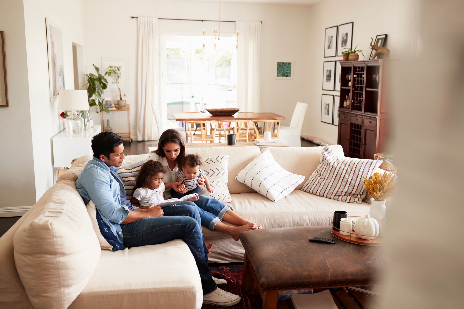 Family sitting together on a beige couch in a bright living room, reading and smiling around a coffee table Family sitting together on a beige couch in a bright living room, reading and smiling around a coffee table