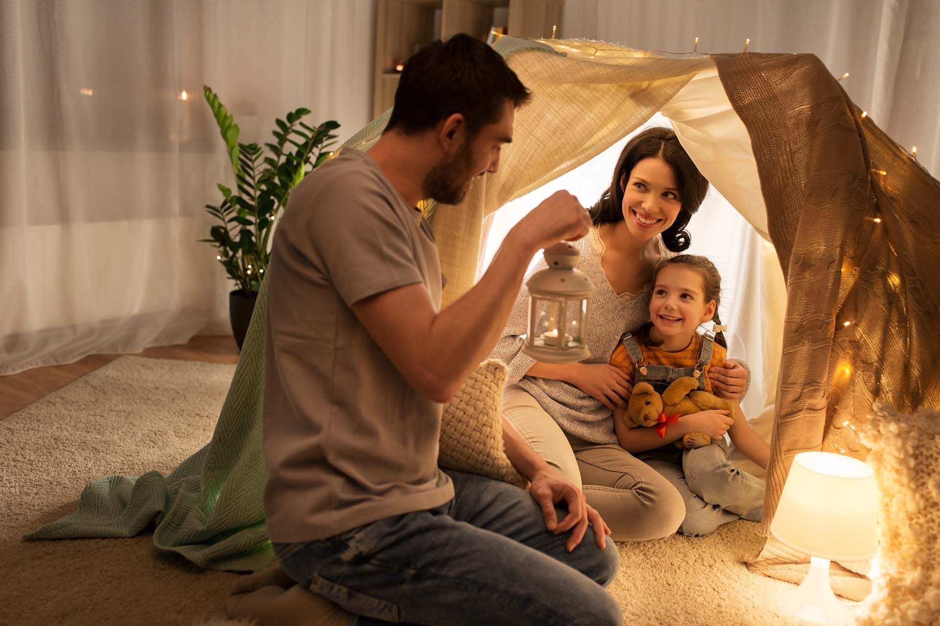 Family reading together inside a cozy blanket fort lit by warm lights. Family reading together inside a cozy blanket fort lit by warm lights.