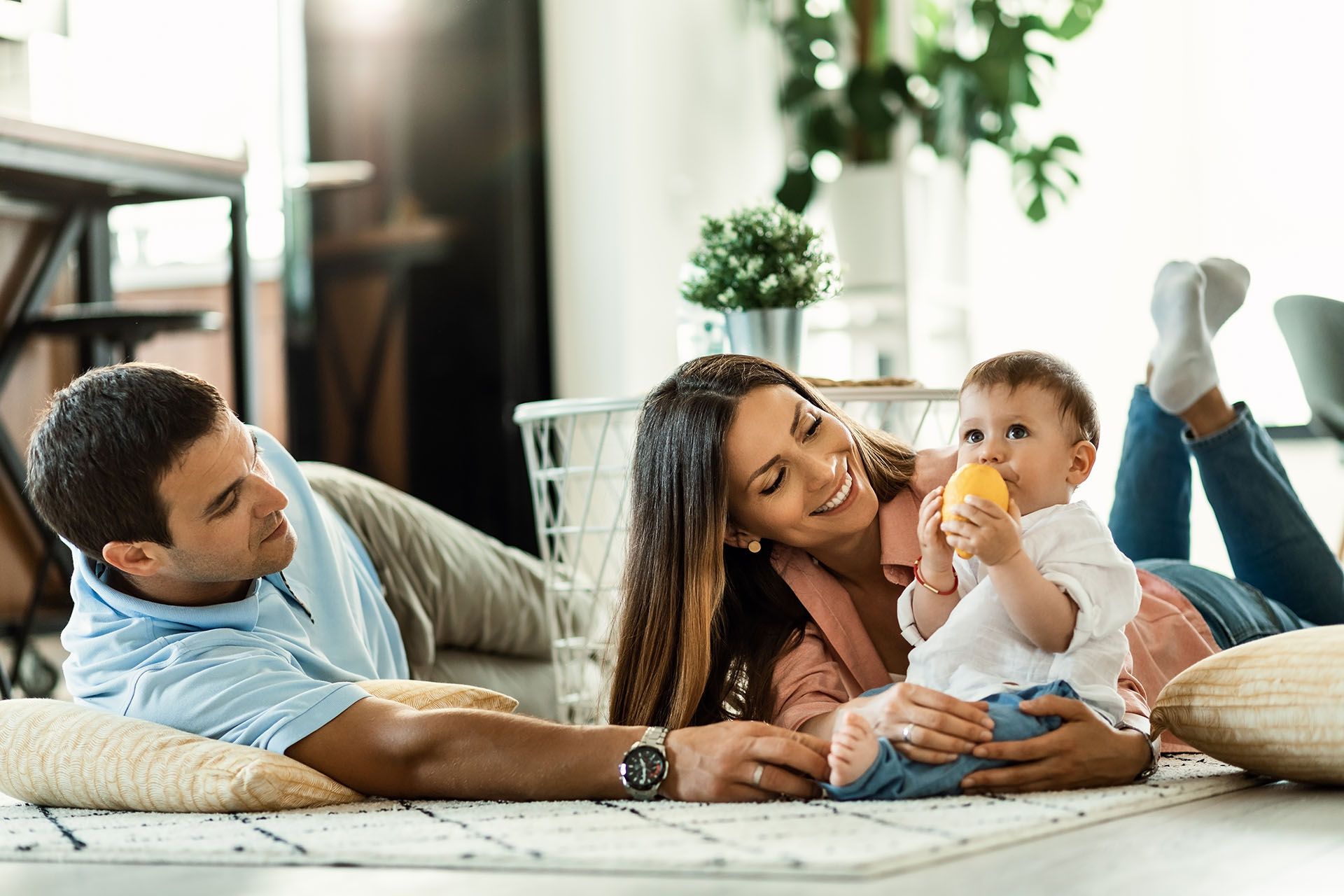 Family relaxing on a couch, smiling with a baby in a bright living room. Family relaxing on a couch, smiling with a baby in a bright living room.