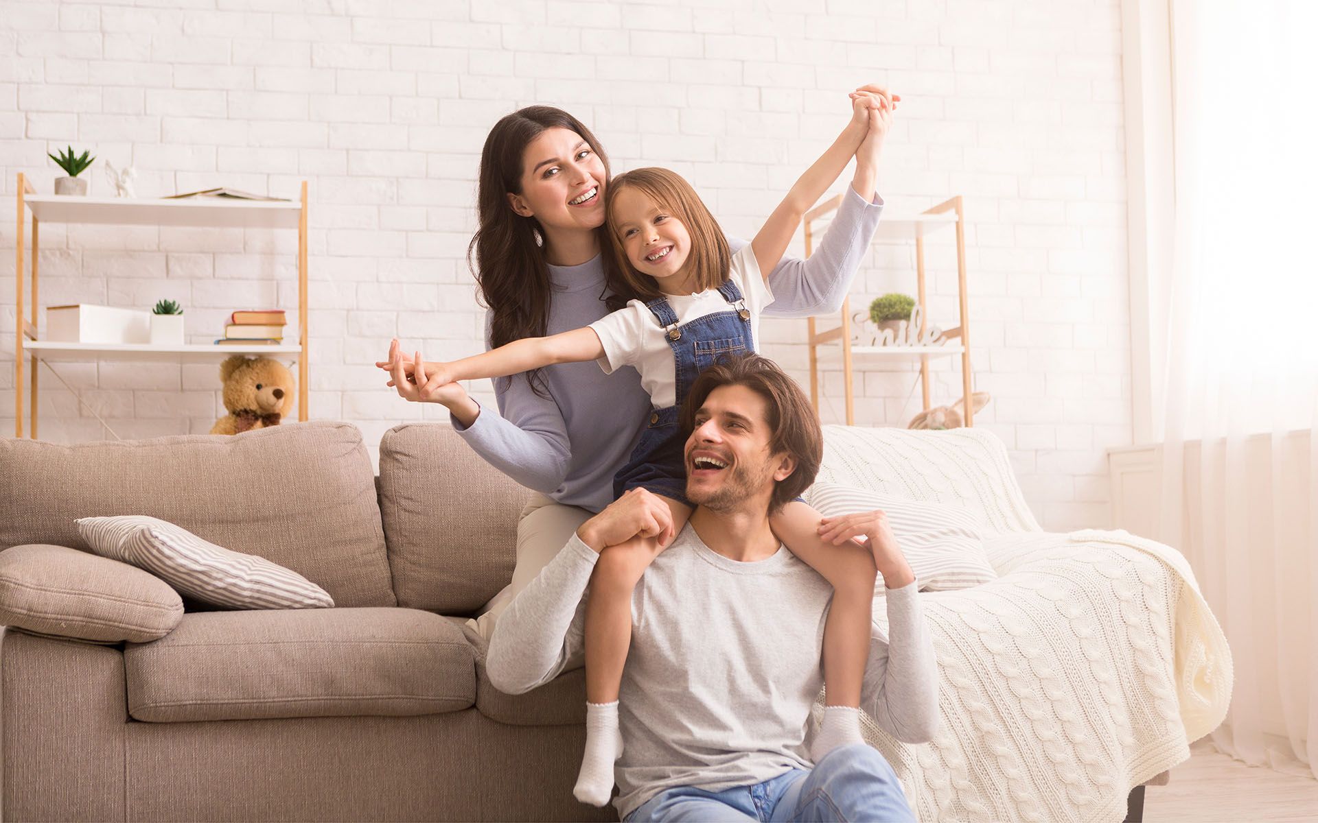 Family relaxing on a beige sofa in a bright living room, smiling and posing together.