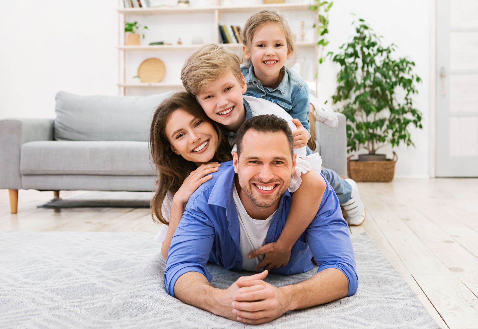 Family of four smiling and stacked on the floor in a bright living room Family of four smiling and stacked on the floor in a bright living room