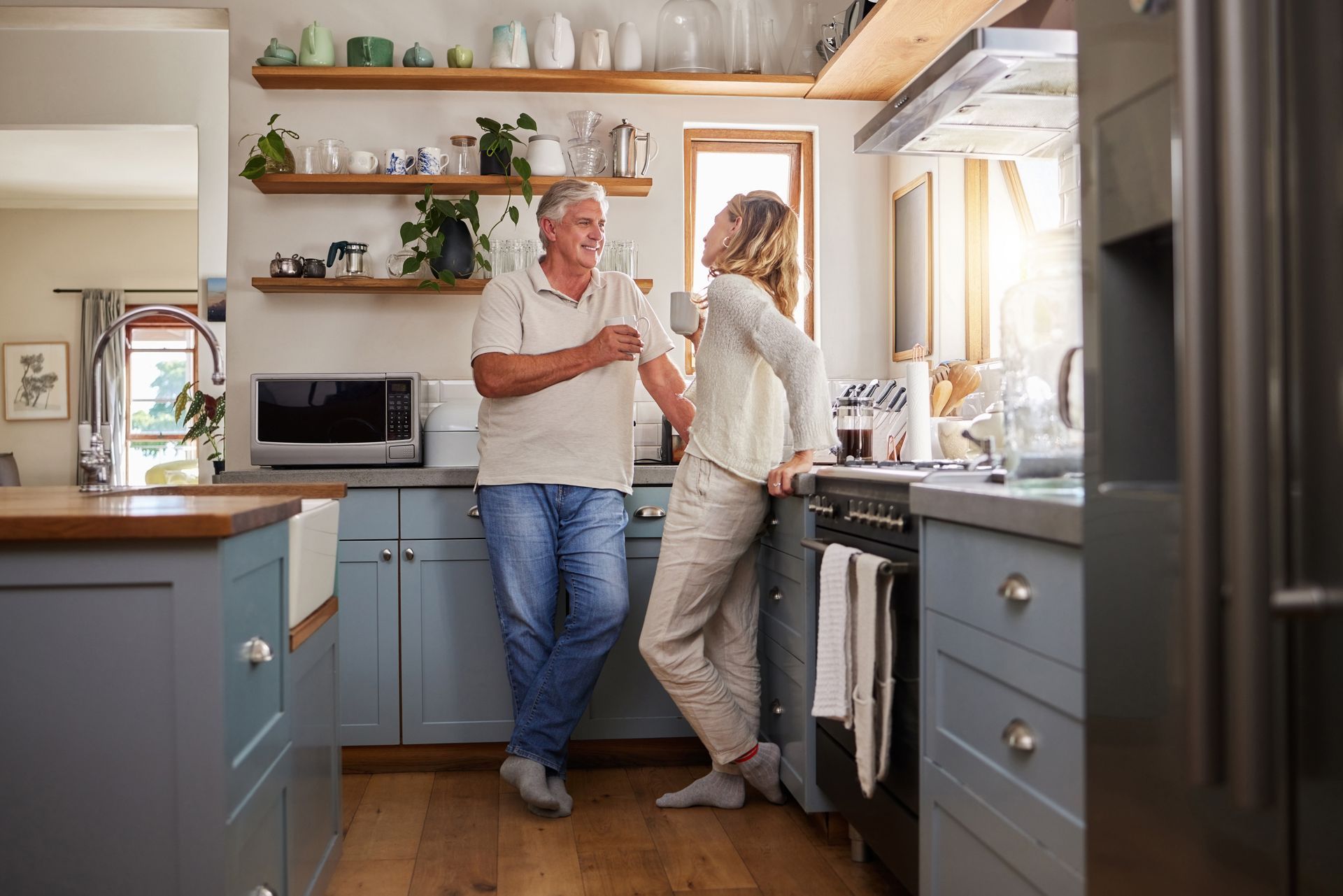 Two people chatting in a bright kitchen with blue cabinets and wooden shelves Two people chatting in a bright kitchen with blue cabinets and wooden shelves