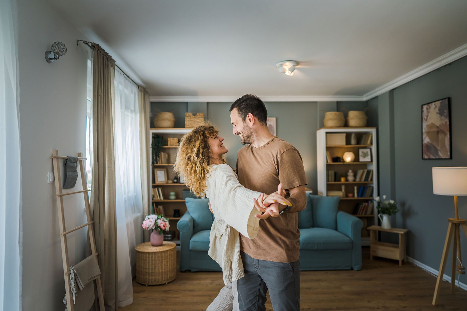 Couple dancing in a cozy living room with a blue sofa and warm lamp light.