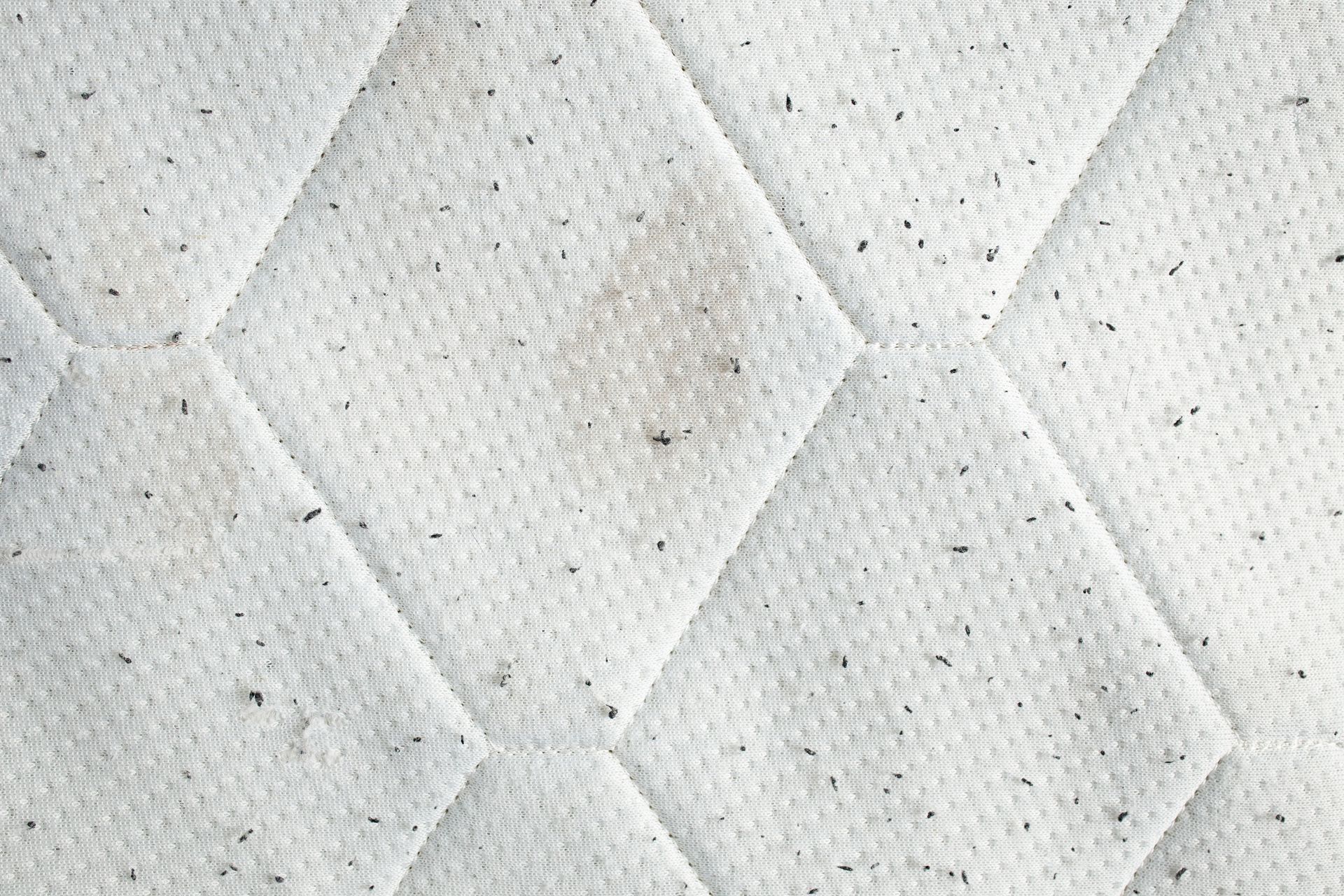 Close-up of a white quilted fabric with diamond stitching and subtle gray speckles.