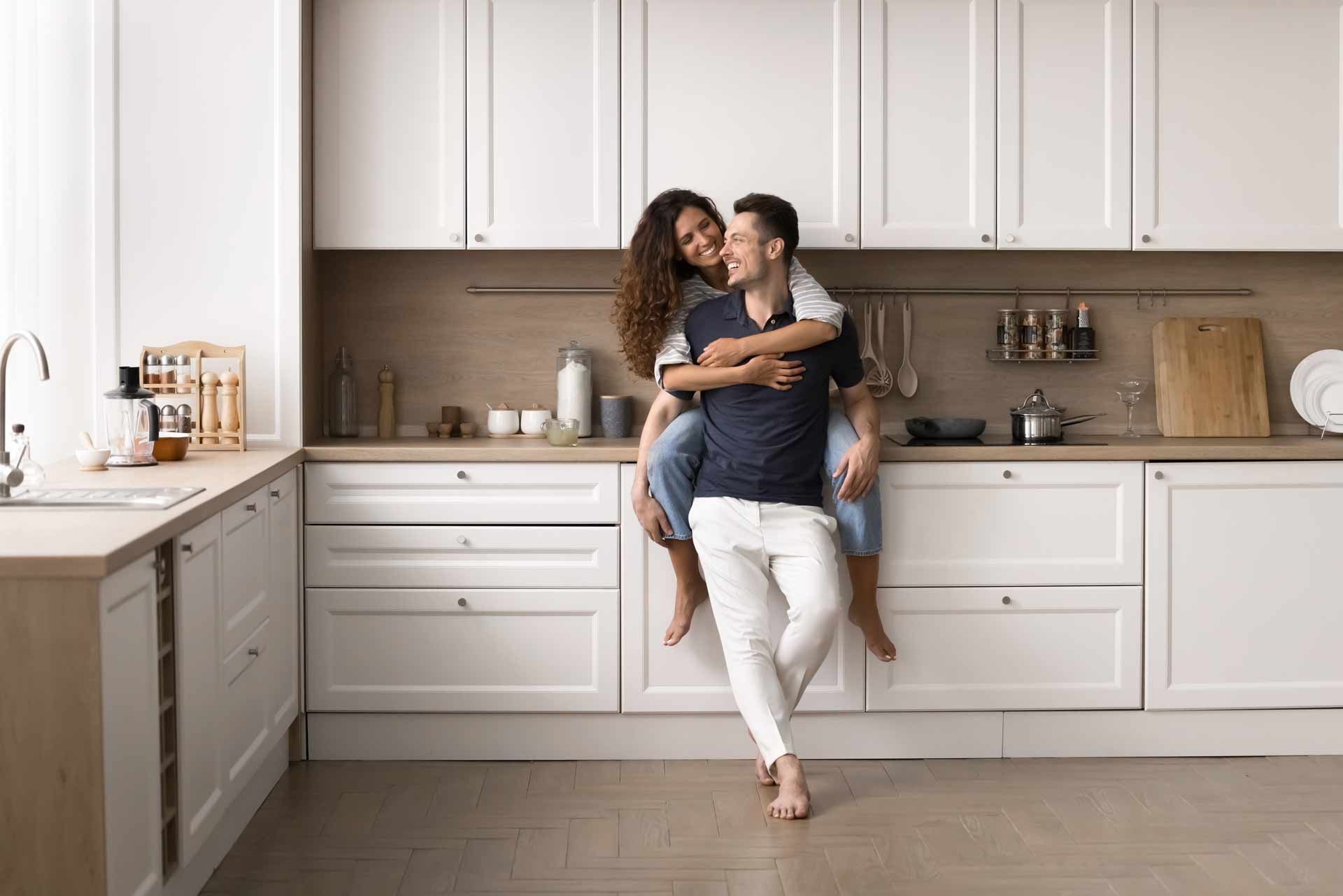 Couple embracing in a bright white kitchen, leaning against the countertop. Couple embracing in a bright white kitchen, leaning against the countertop.