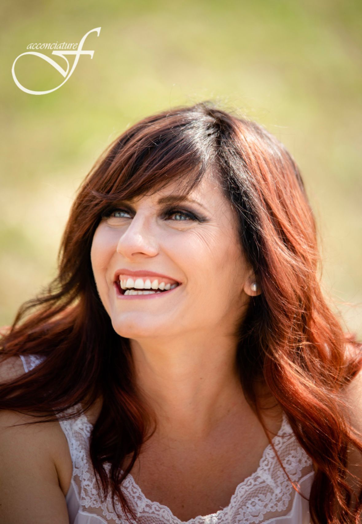 Donna sorridente con lunghi capelli ramati all'aperto, su uno sfondo verde tenue.