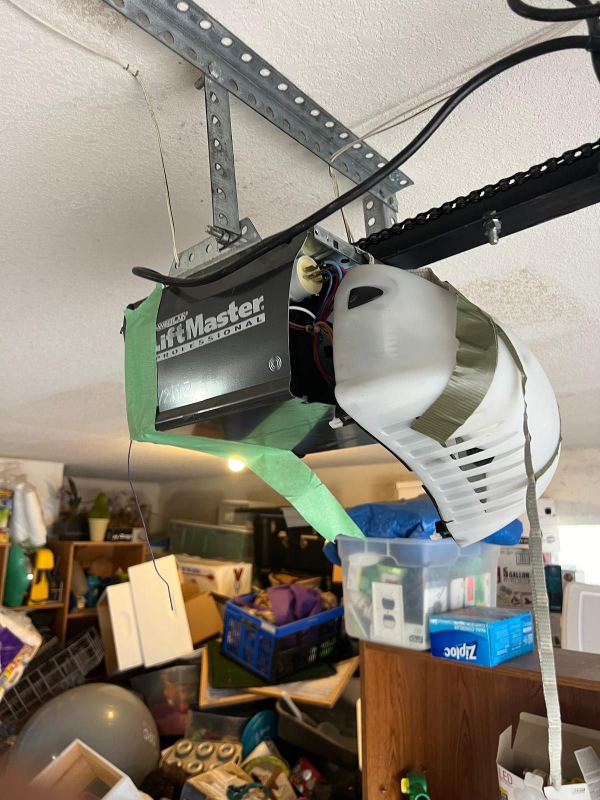 Garage door opener with exposed internal components, green and white casing, mounted on ceiling.