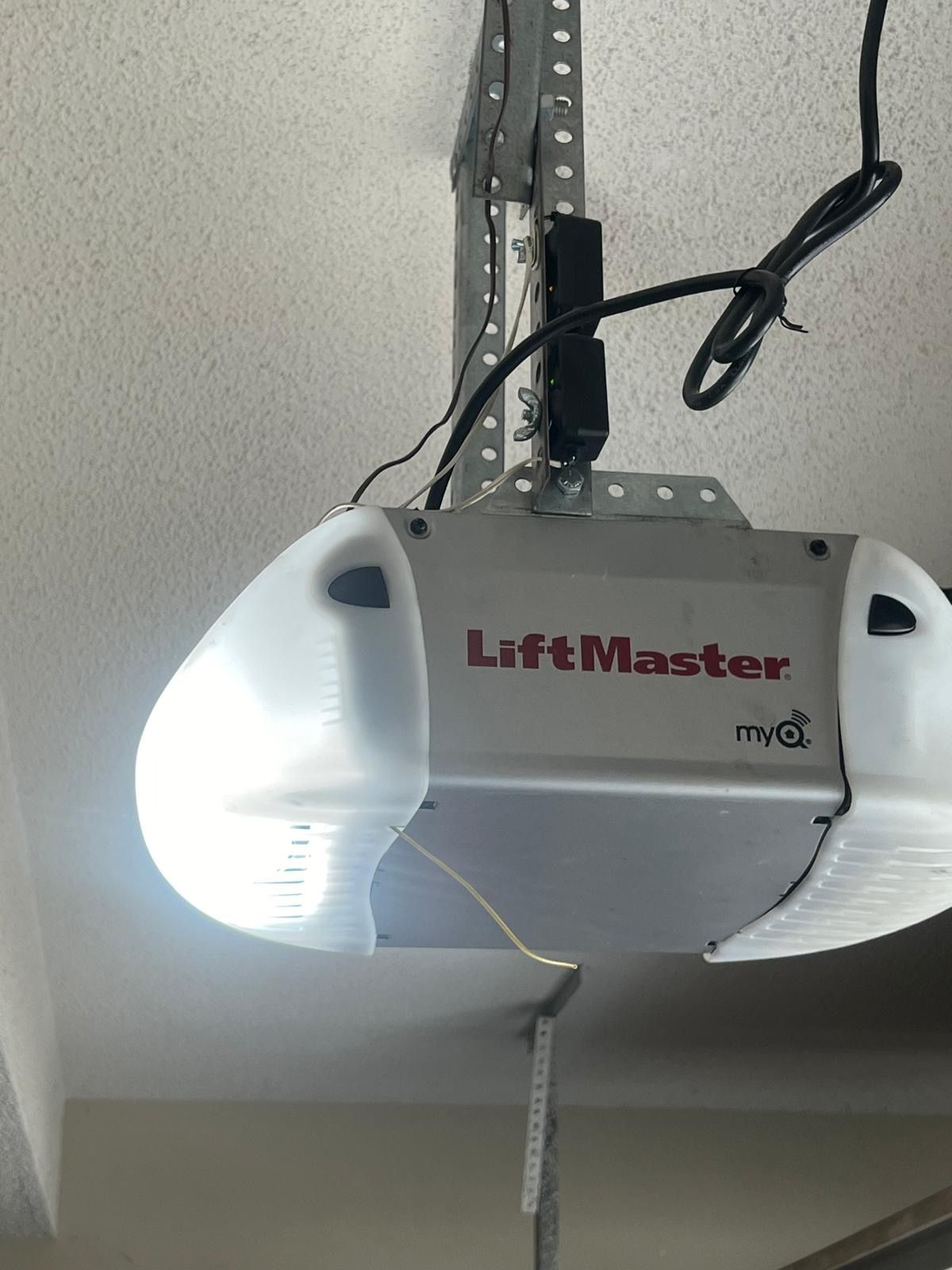 LiftMaster garage door opener mounted on a ceiling.  Unit is silver with white light covers; one light is on.